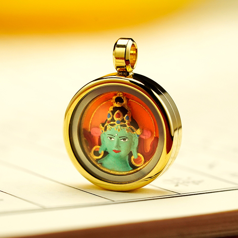 Gold pendant with a green deity figure on a reflective surface